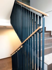 Interiérové schodišťové ocelové zábradlí PTROWERK zhotovené z ploché kolmo orientované ocele. Madlo zábradlí dubové.